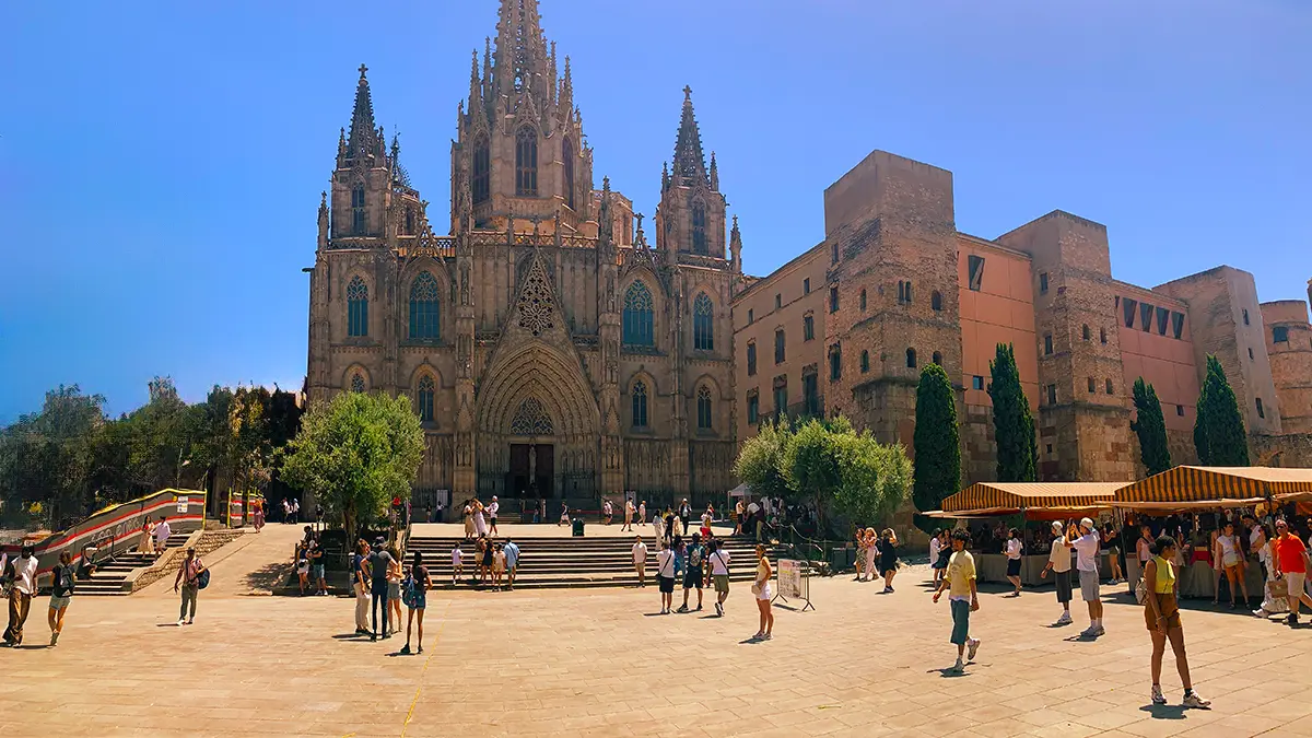 Wide view of Plaça de la Seu with Barcelona Cathedral and many tourists under blue skies on the Barcelona Gothic Quarter & Coast Bike Tour.