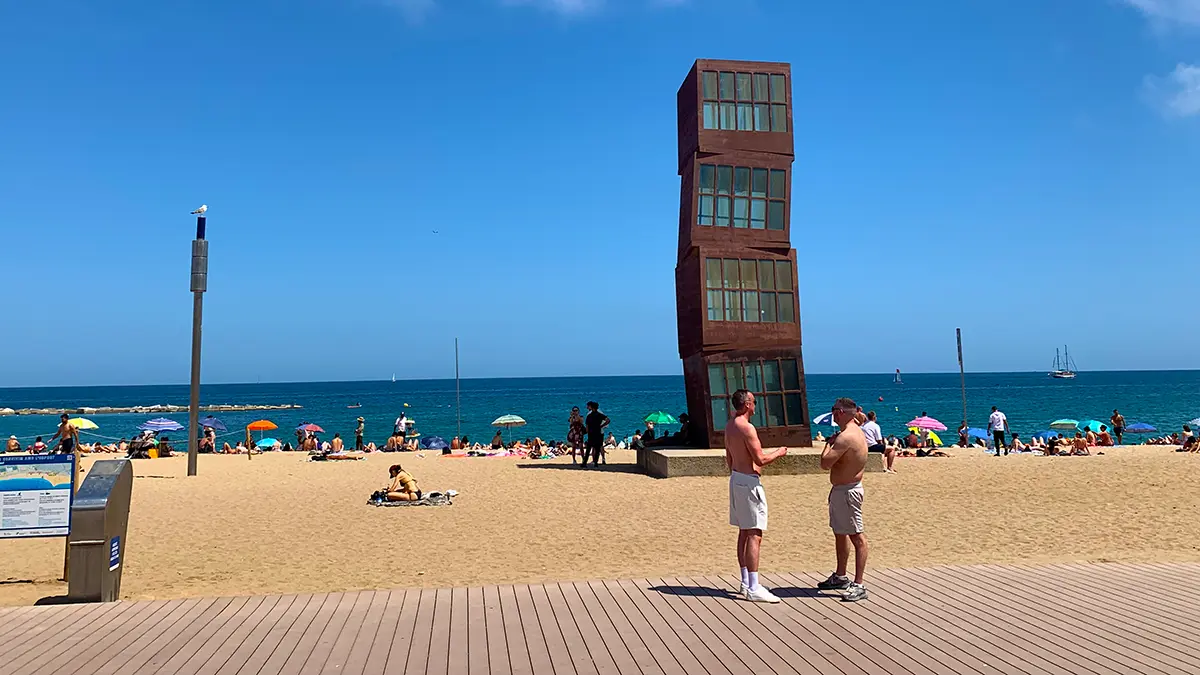 People enjoying Barceloneta beach with the iconic W Hotel sculpture (Peix) in the background during the Barcelona Gothic Quarter & Coast Bike Tour.