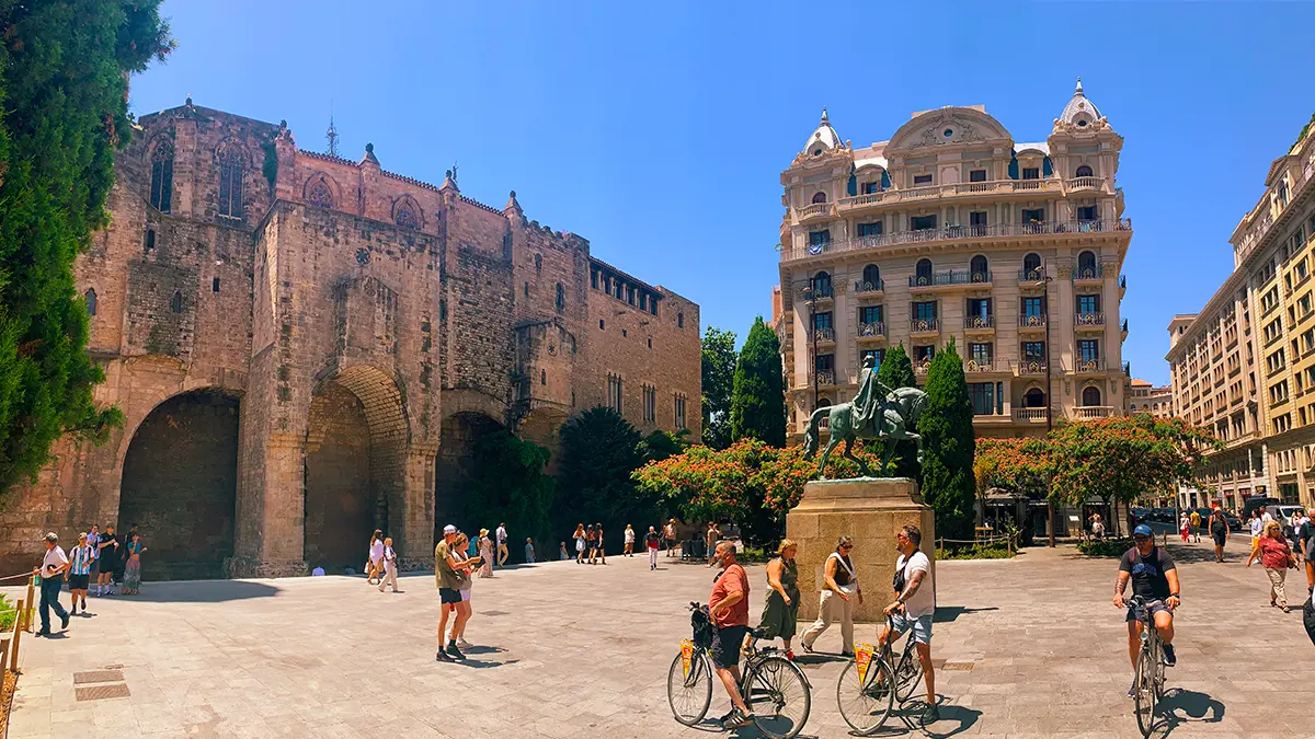 Cyclists riding past ancient Gothic walls and a statue of Ramon Berenguer III on the Barcelona Gothic Quarter & Coast Bike Tour.