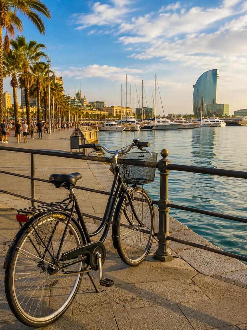 Classic bicycle parked along the marina promenade at Port Vell with palm trees, yachts, and the W Barcelona hotel glowing in late-afternoon light during Barcelona in September.