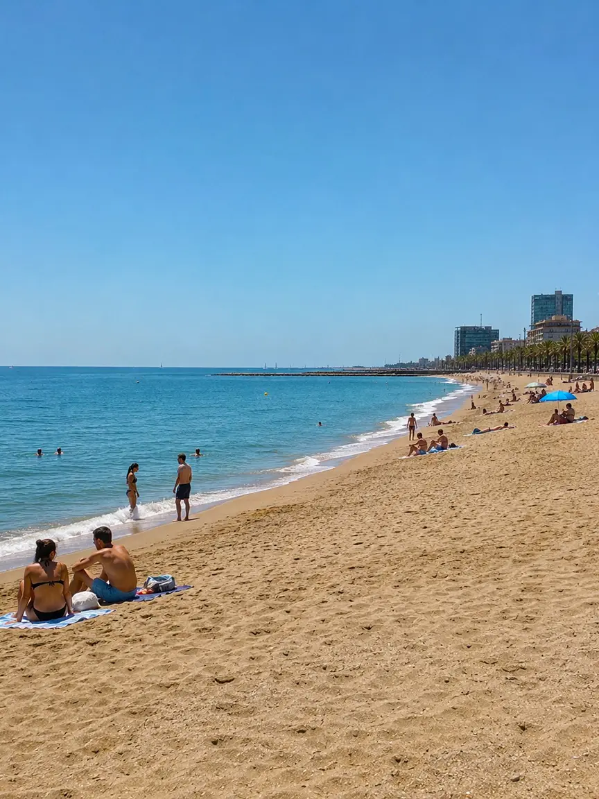 Wide sandy beach with people swimming and sunbathing under a clear blue sky in Barcelona in September.