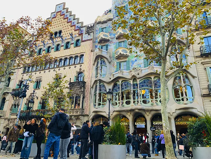 Casa Batlló on Passeig de Gràcia in Barcelona, a colorful Gaudí-designed house with mosaic façade, curved balconies, large windows, and crowds of visitors in front.