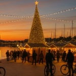 A vibrant Christmas market at Port Vell harbor during sunset, featuring a massive illuminated Christmas tree with golden lights and a shining star, wooden stalls adorned with fairy lights, crowds of people shopping, and cyclists riding along the waterfront promenade, capturing the festive atmosphere of Christmas cycling in Barcelona 2026.