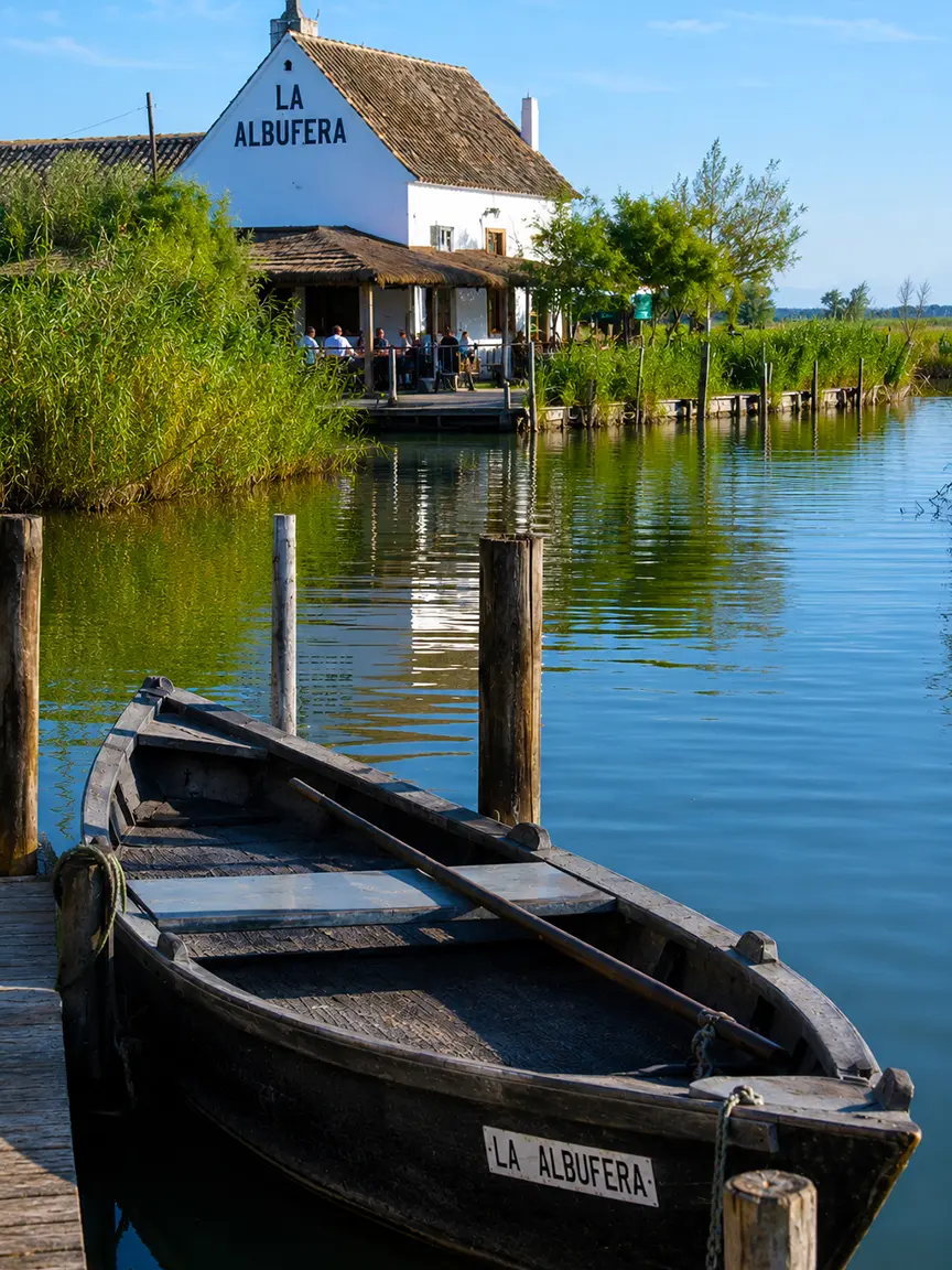 Traditional wooden boat on the calm waters of La Albufera near Valencia, with a scenic restaurant and reeds in the background, Gay Games Valencia 2026.