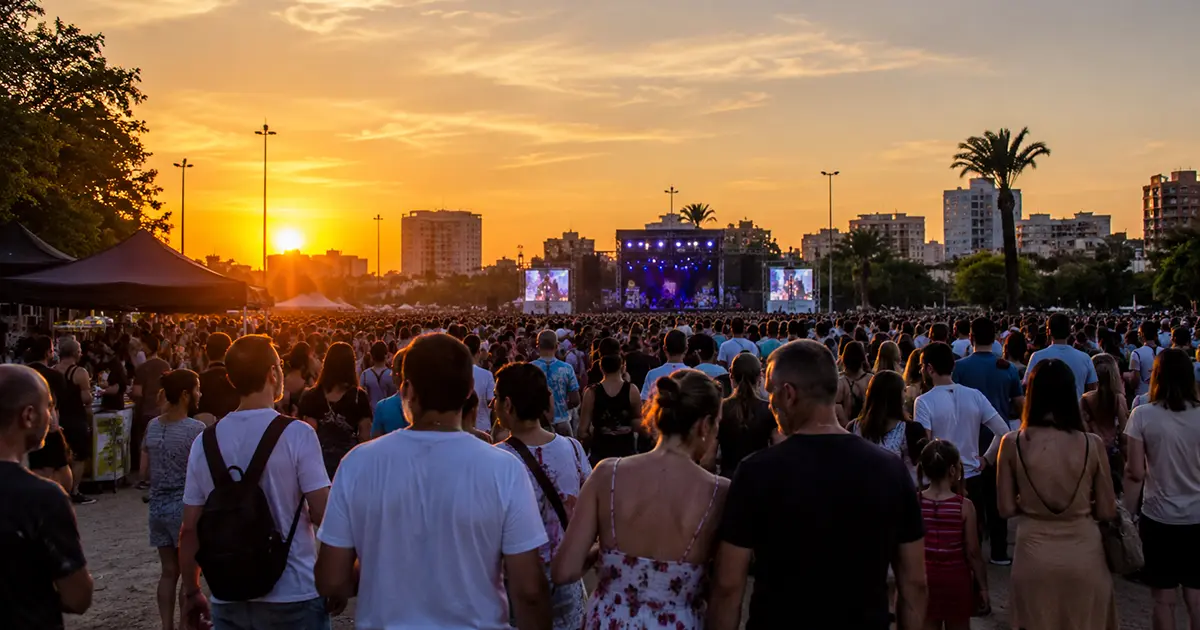 Vibrant crowd enjoying a live concert at sunset during Macromascletà Universal Valencia 2026, with a brightly lit stage against the orange sky and city skyline.