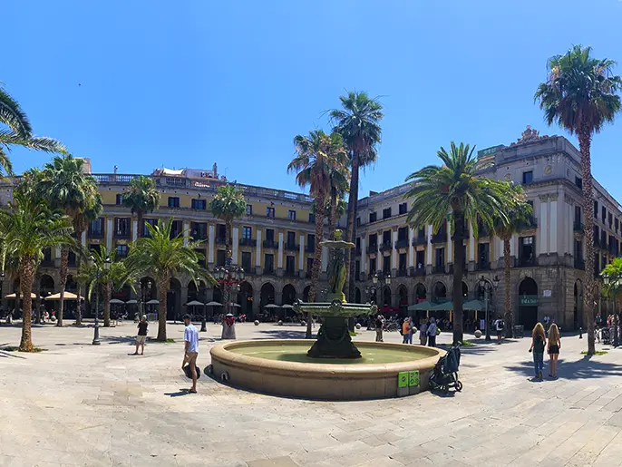Beautiful Plaça Reial with central fountain and palm trees on a bright day.