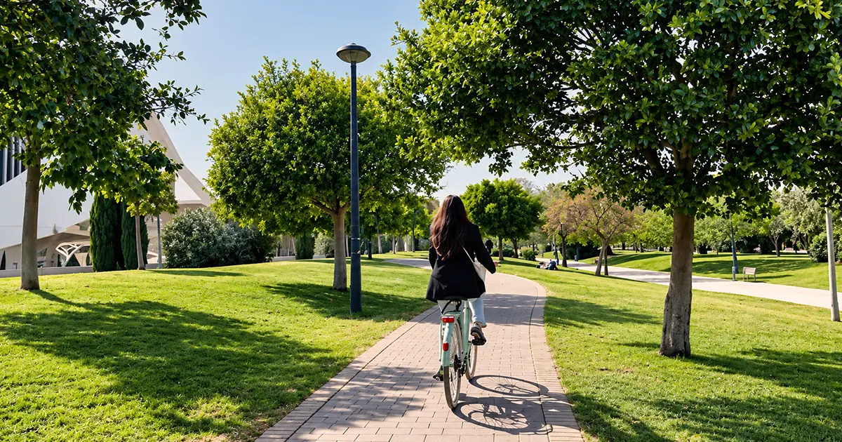 Woman cycling along a tree-lined path in Turia Gardens Valencia on a sunny day.