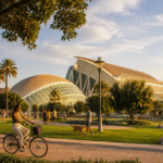 Sunny park scene in Valencia in September with people cycling, walking dogs, and relaxing on the grass in front of the City of Arts and Sciences complex at golden hour.