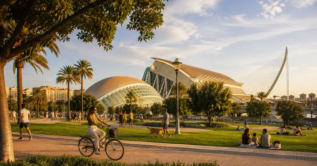Sunny park scene in Valencia in September with people cycling, walking dogs, and relaxing on the grass in front of the City of Arts and Sciences complex at golden hour.